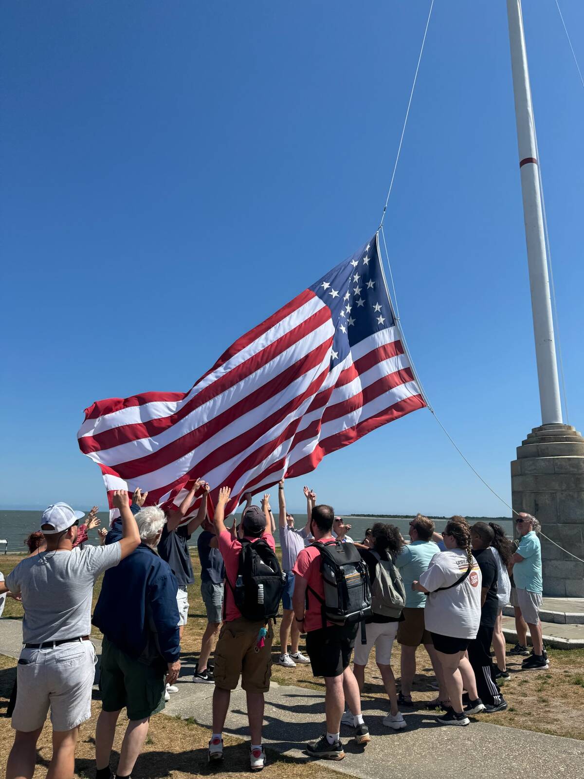 Visitors raising their hands to catch the flag during the flag-lowering ceremony at Fort Sumter, Charleston Harbor behind them